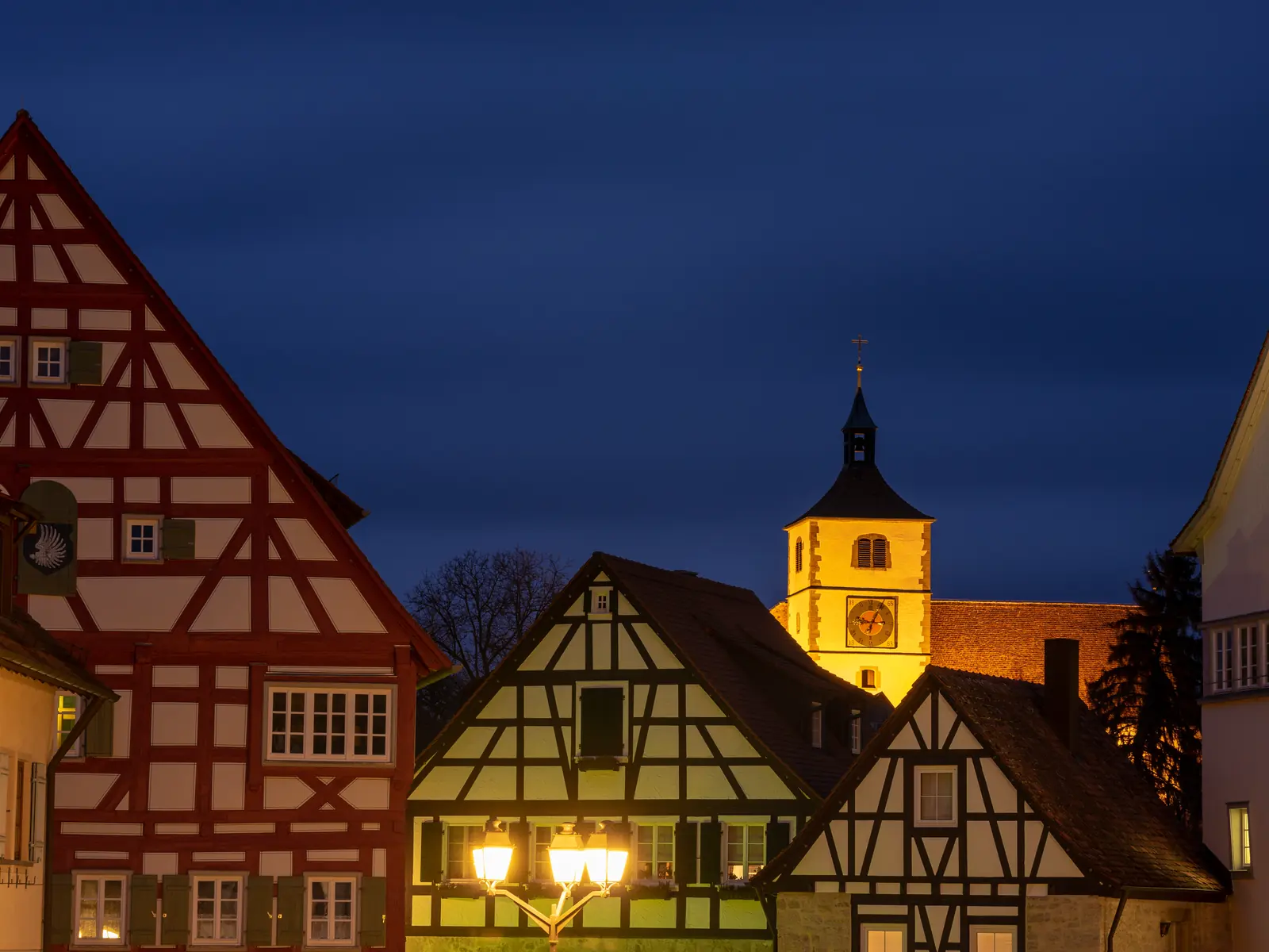 Half-timbered houses on the market square of Vellberg at blue hour, with a lit church tower behind them